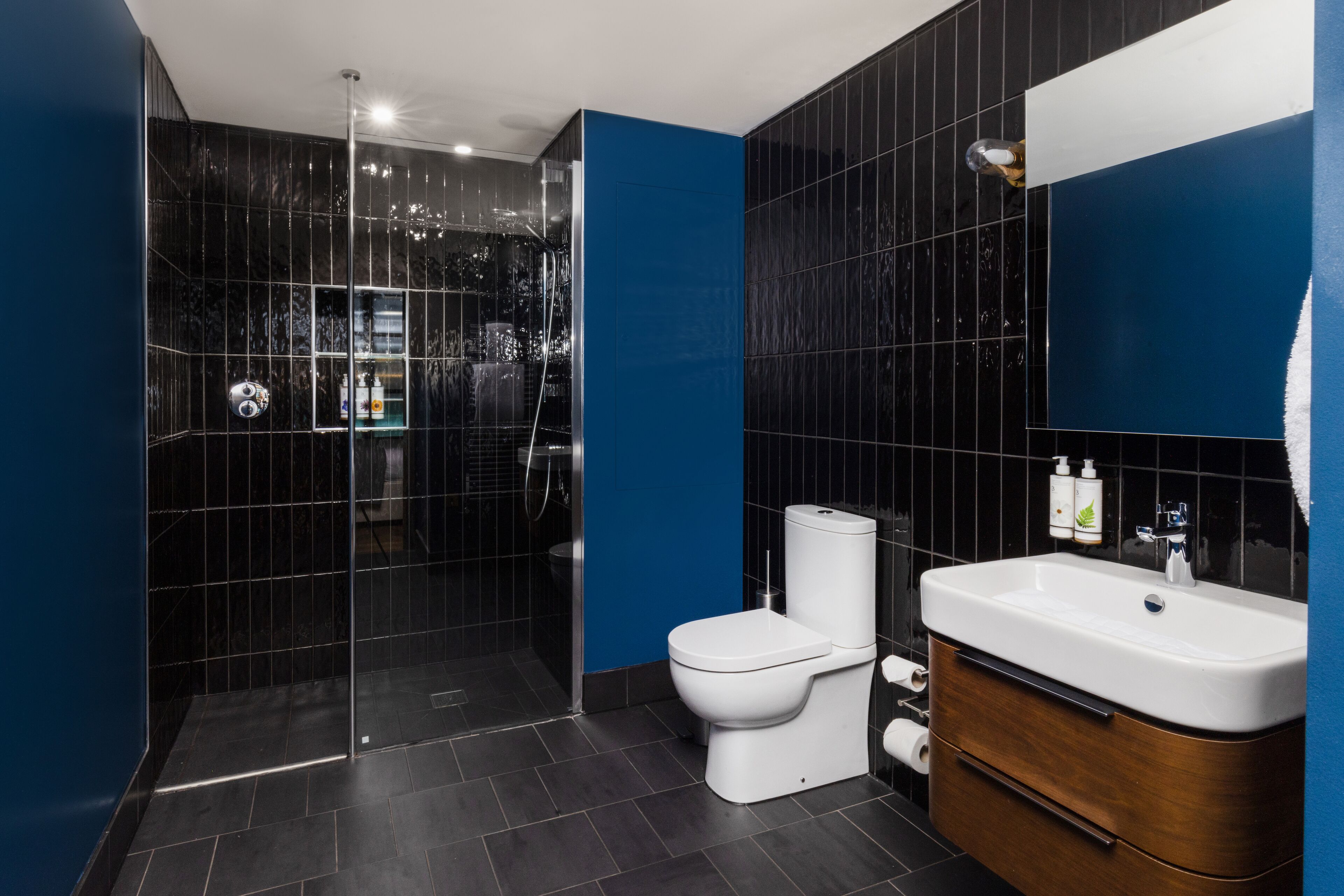 A modern bathroom with a glass-enclosed shower, a white toilet, and a wooden vanity with a sink.