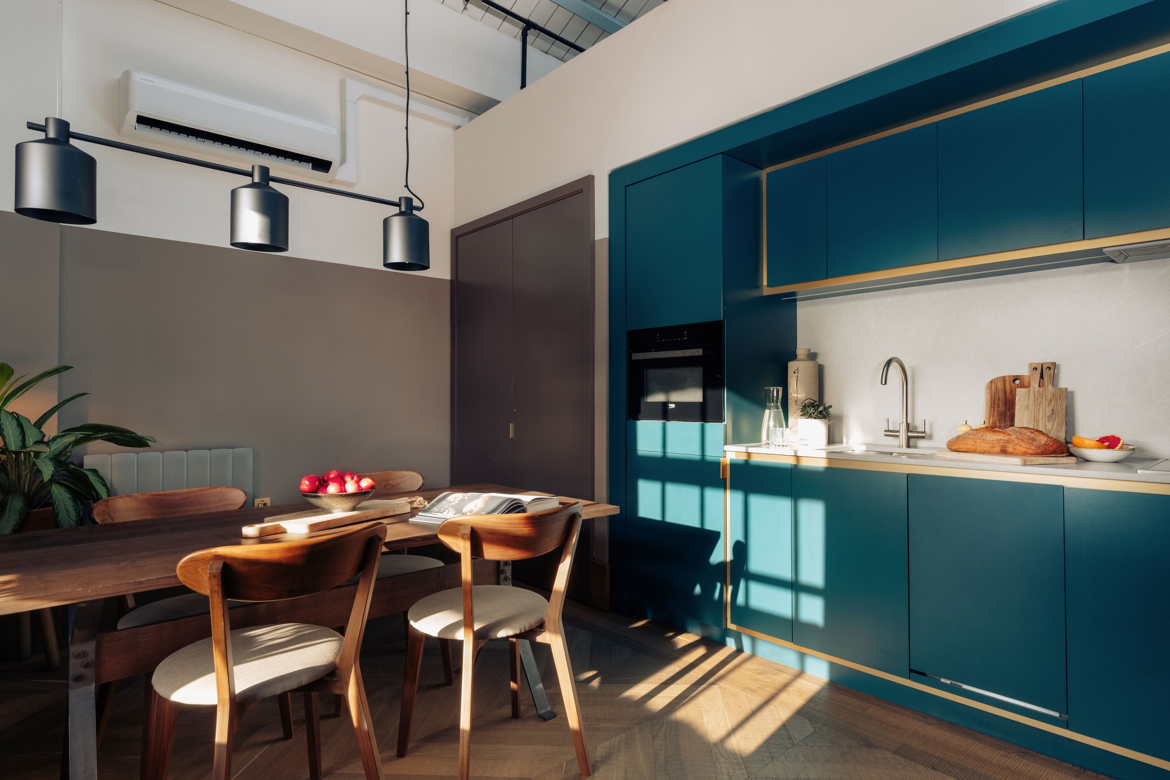 Een moderne keuken met blauwgroene kastjes, een houten eettafel en hanglampen.