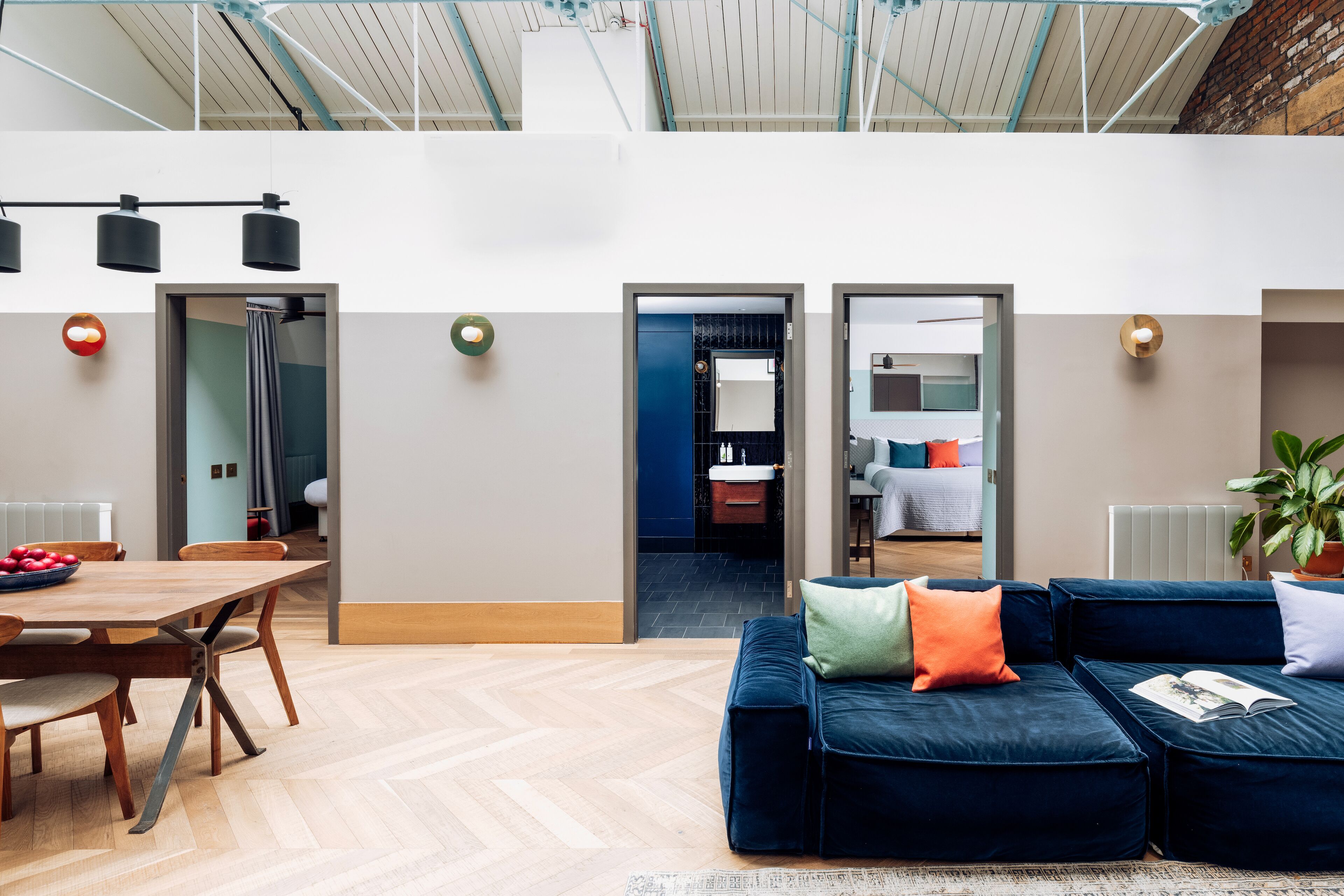 A modern interior with a dining area, a blue sofa, and a kitchen visible through an open door.