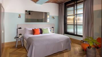 Quarto moderno com uma cama grande, um espelho acima, uma janela com cortinas, uma mesinha com uma planta e uma cadeira.