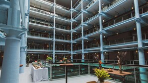 A multi-level atrium with glass railings, tables with floral centerpieces, and a high ceiling with exposed beams. - Native Manchester (Manchester)
