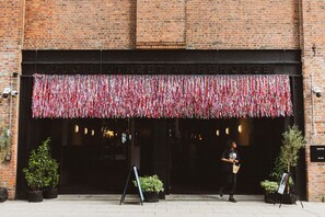 A brick building with a sign reading "DUCIE STREET WAREHOUSE". There are potted plants outside and a person walking by.