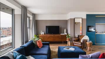A modern living room with a large window, a flat-screen TV, a brown leather armchair, and a blue sofa set.