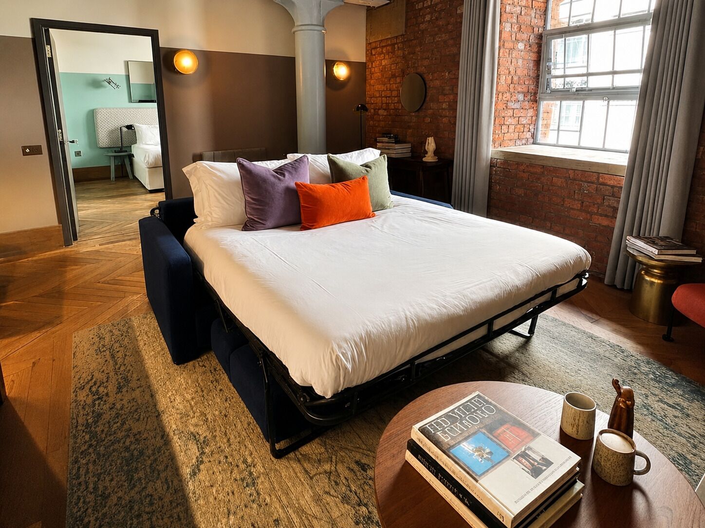 Habitación de hotel moderna con una cama grande, una mesa de centro redonda y vistas a la ciudad.
