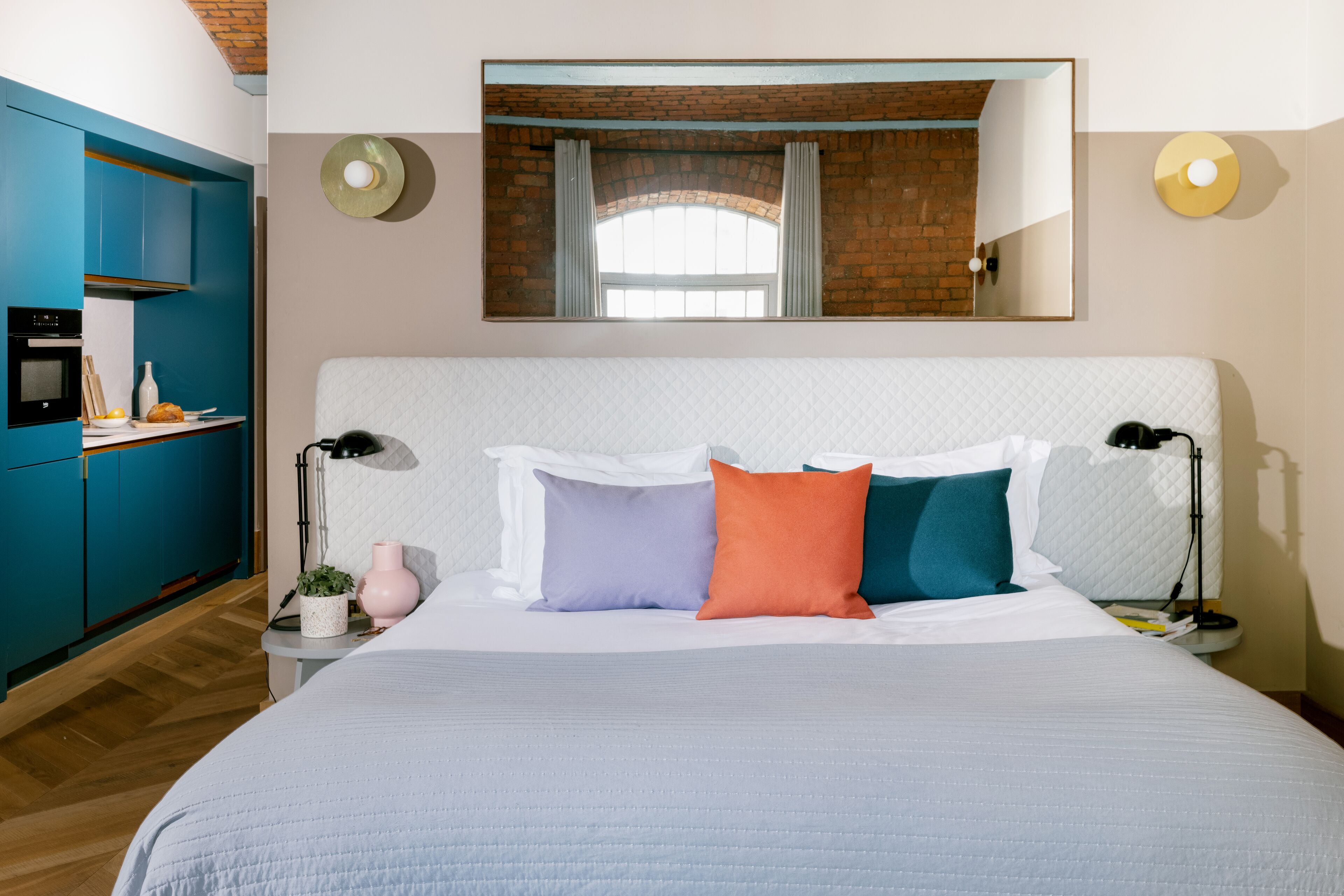 Une chambre avec un grand lit, un coin cuisine et un miroir au mur.