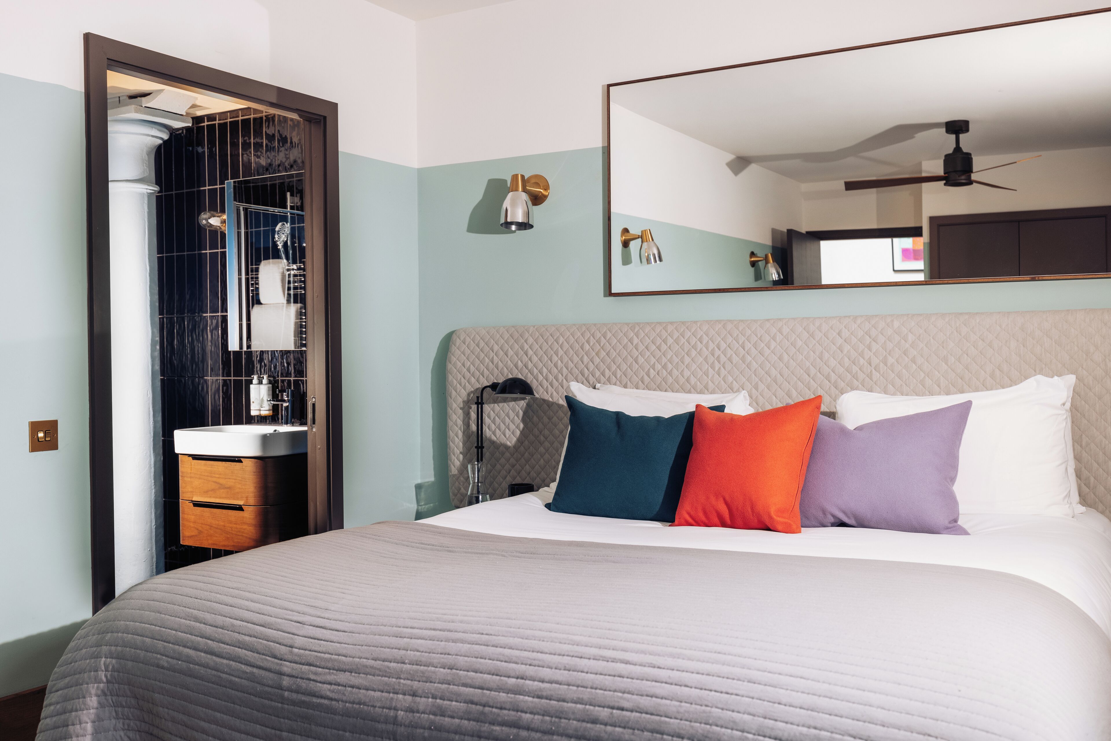 A hotel room with a large bed, a bedside table, a mirror, and a bathroom visible through an open door.