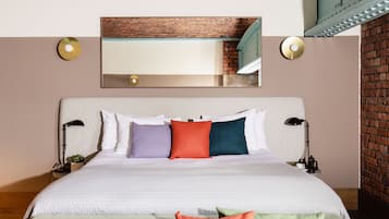 A neatly made bed with a white headboard, multiple pillows in various colors, two bedside lamps, and a small plant on the nightstand.