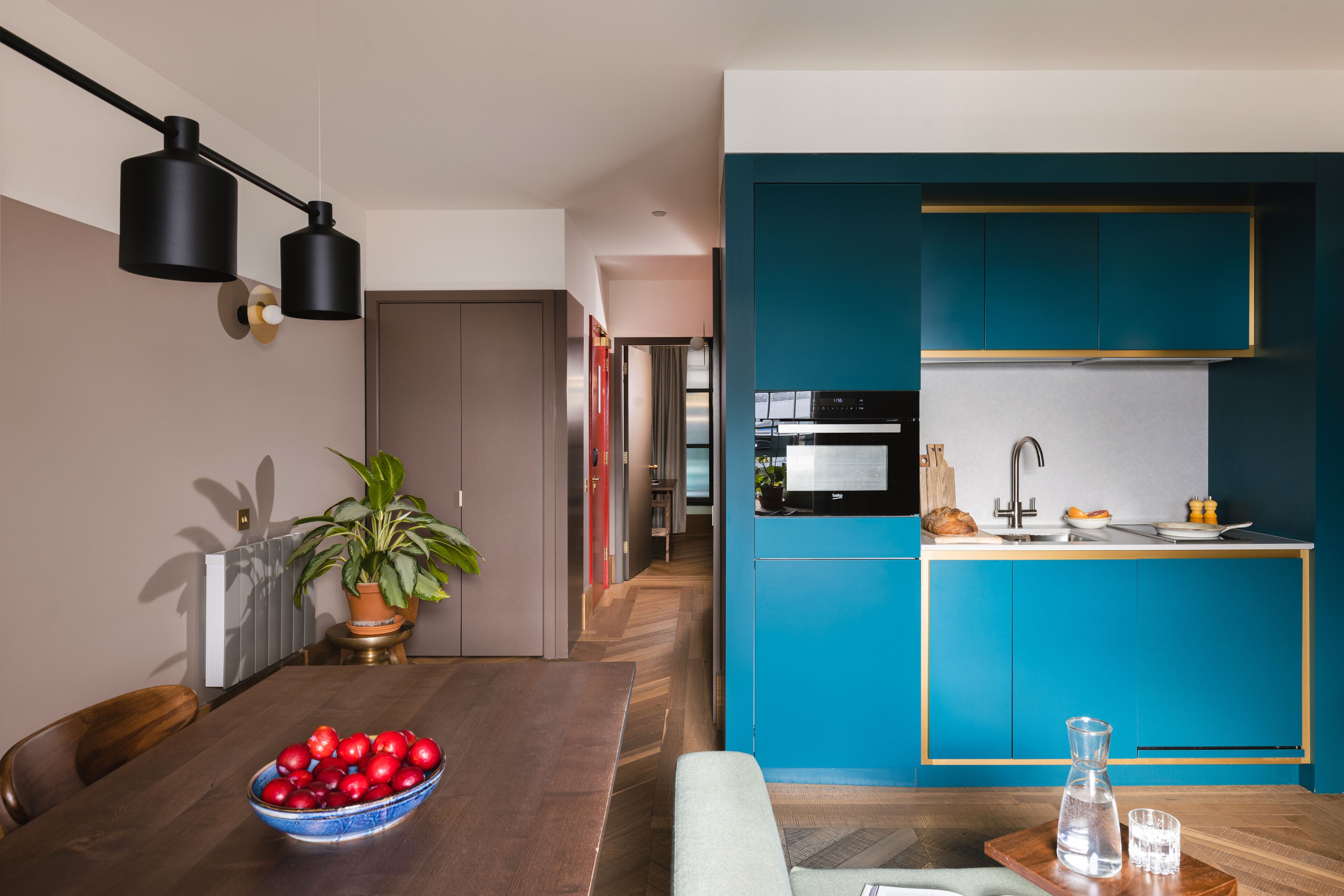 A modern kitchen with teal cabinetry and a wooden countertop.