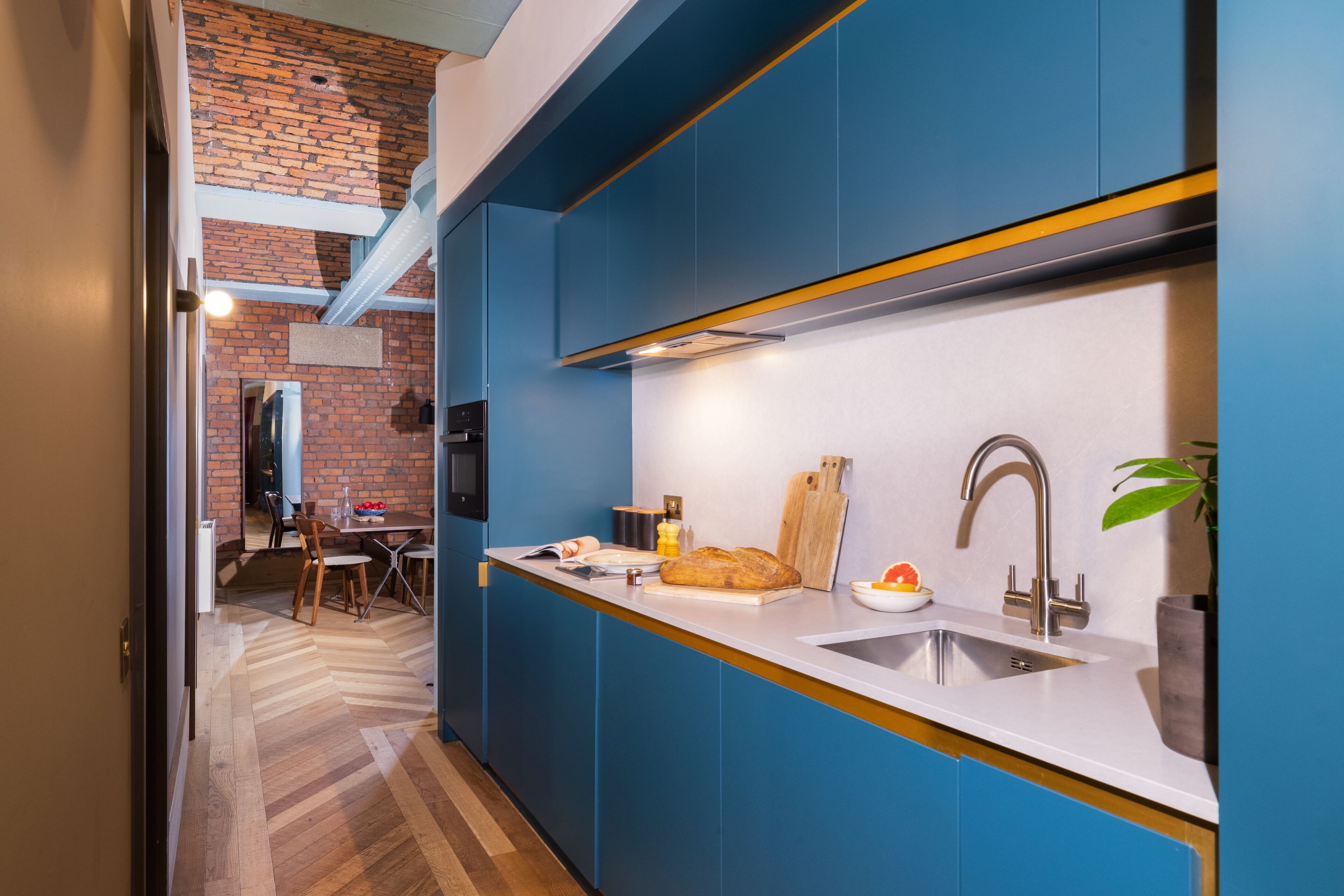 A modern kitchen with blue cabinets, a white countertop, and a brick wall in the background.