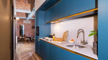 A modern kitchen with blue cabinets, a white countertop, and a brick wall in the background.