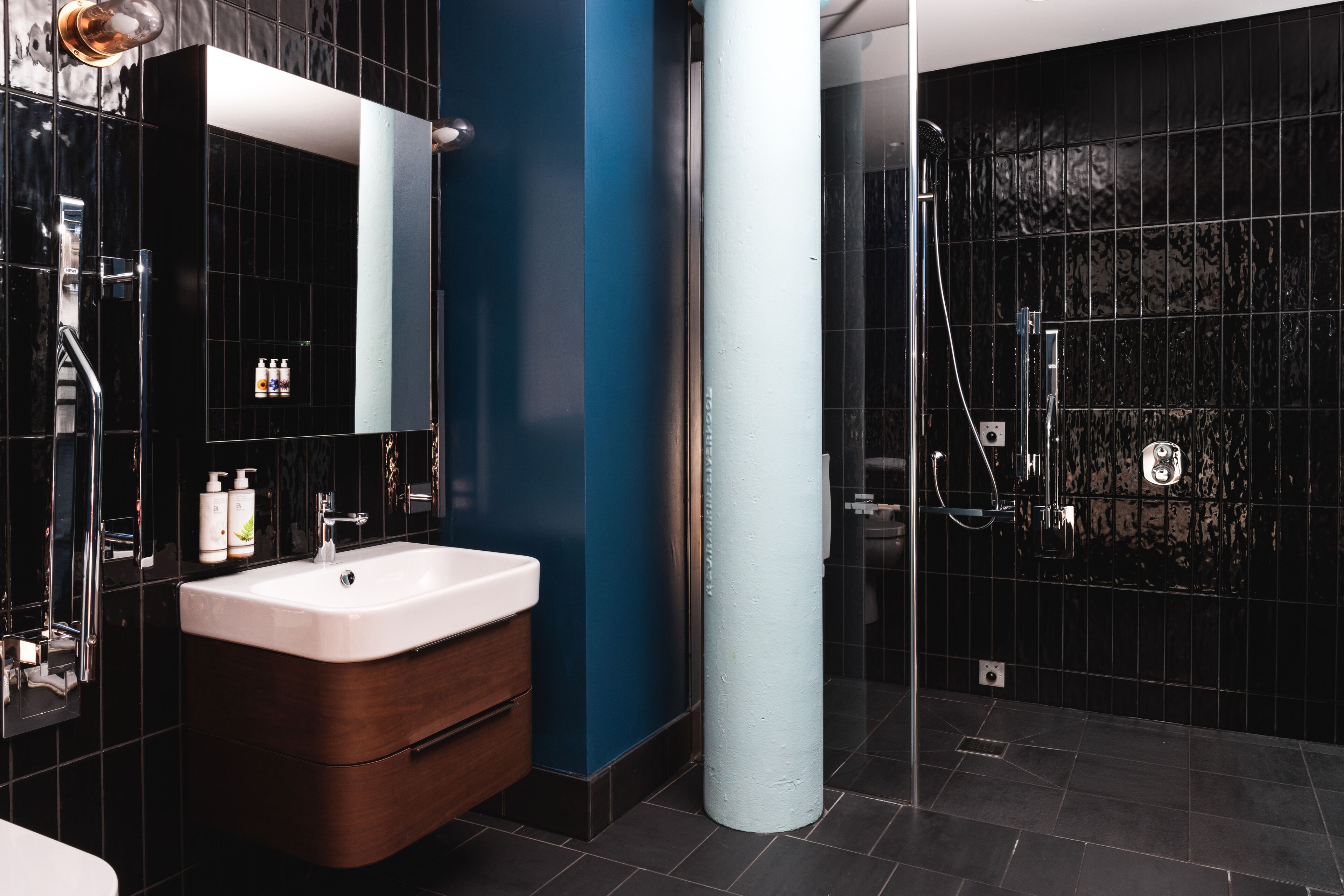A modern bathroom with a large mirror, a white sink, and a dark tiled shower area.