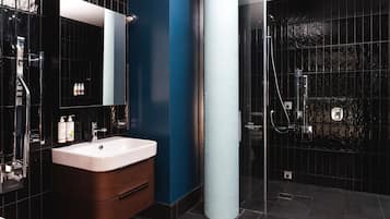 A modern bathroom with a large mirror, a white sink, and a dark tiled shower area.