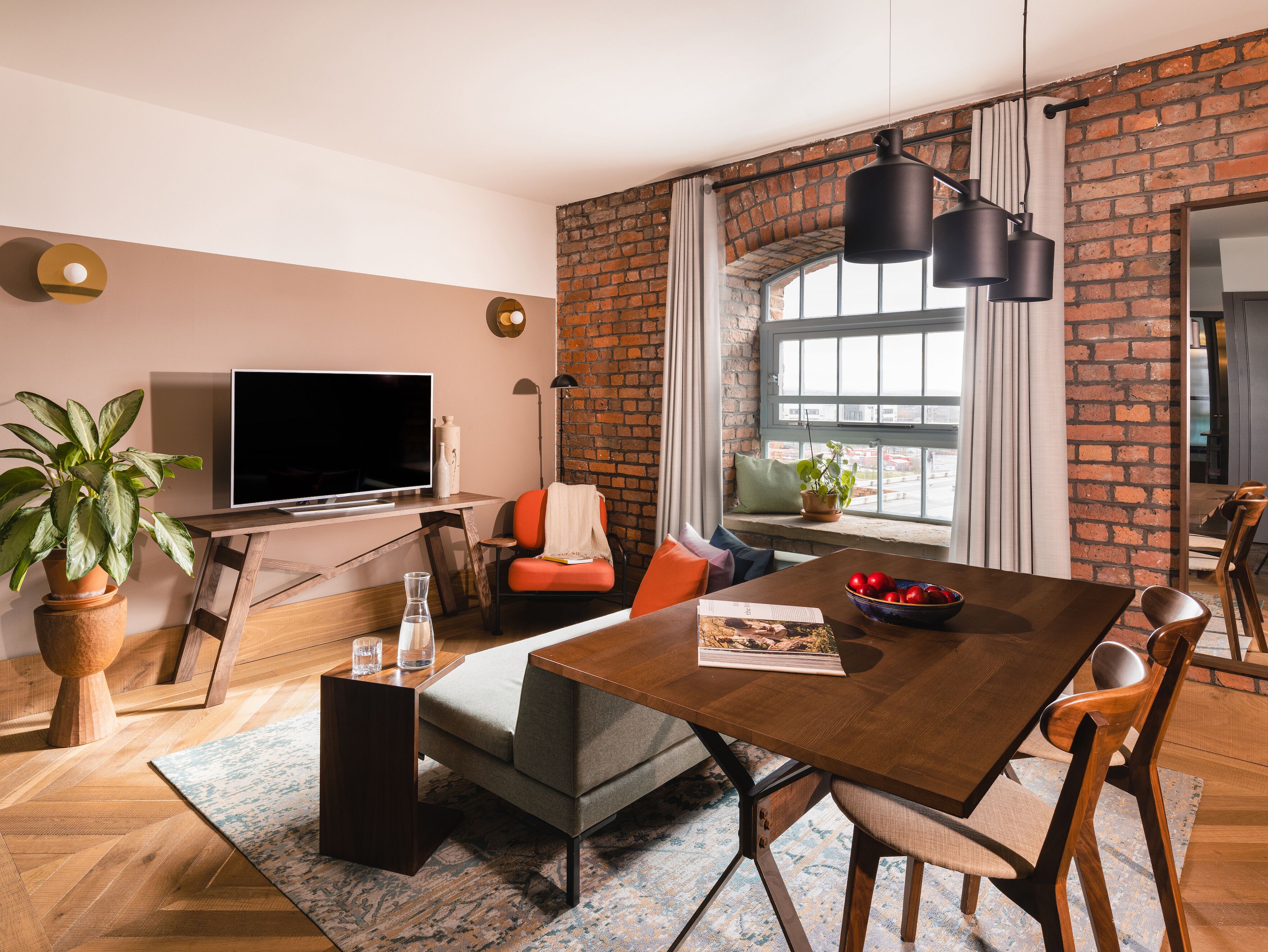 Un salon moderne avec un mur en briques, une grande fenêtre, une table à manger et un téléviseur.