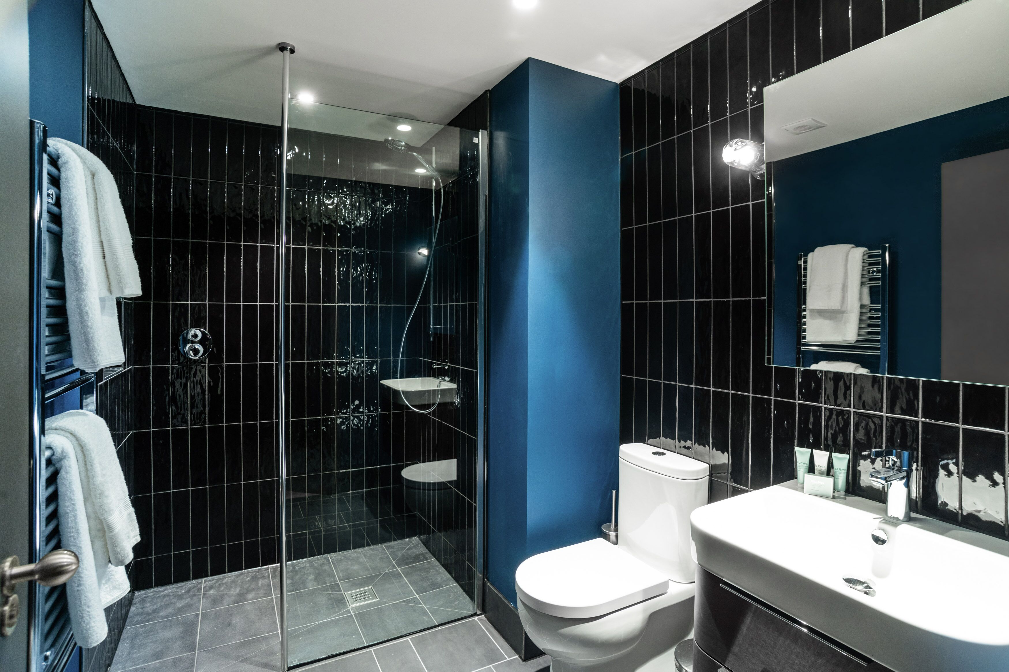 A modern bathroom with a glass-enclosed shower, a white toilet, and a sink with a mirror.