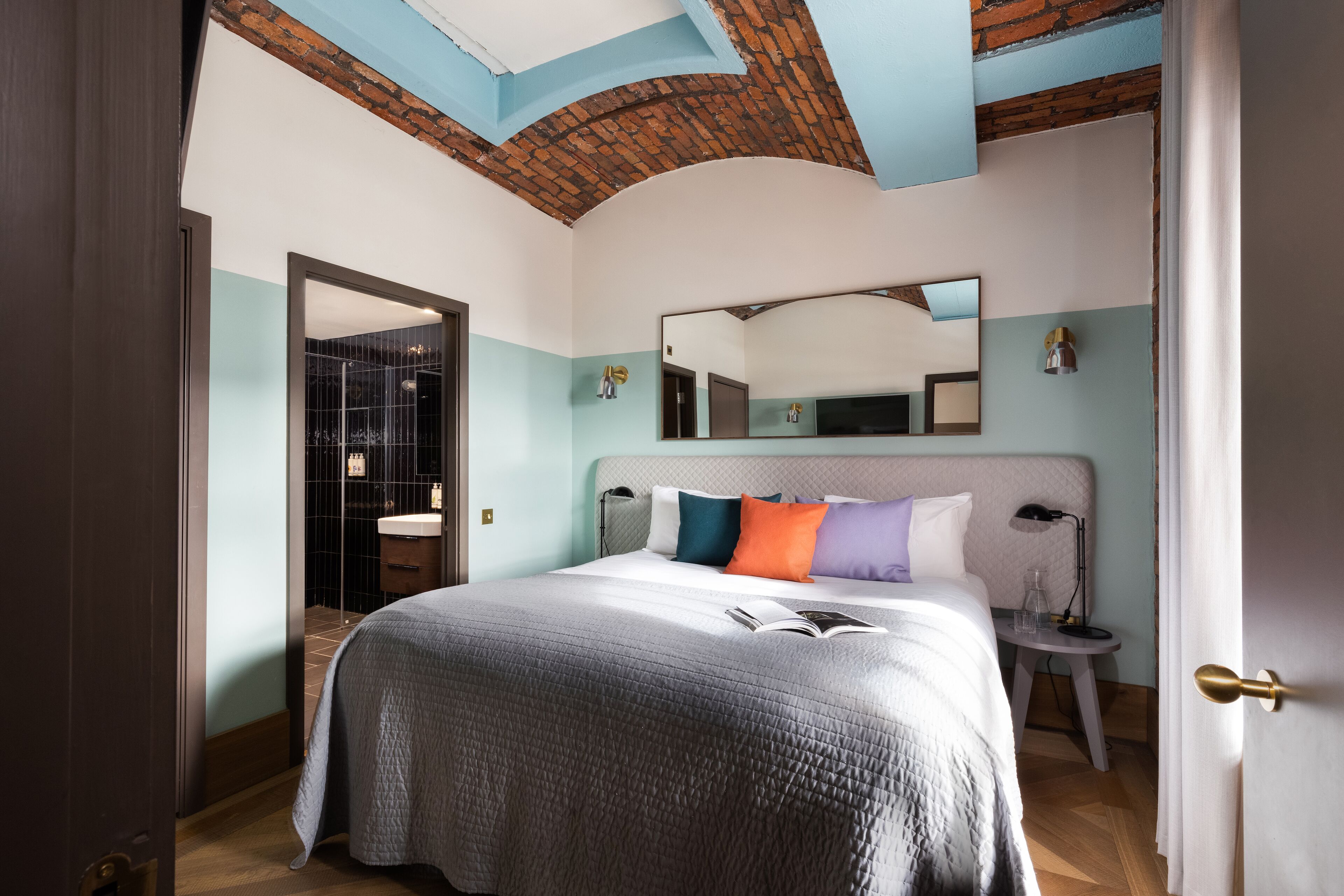 A hotel room with a large bed, a bedside table, a mirror, and a door.