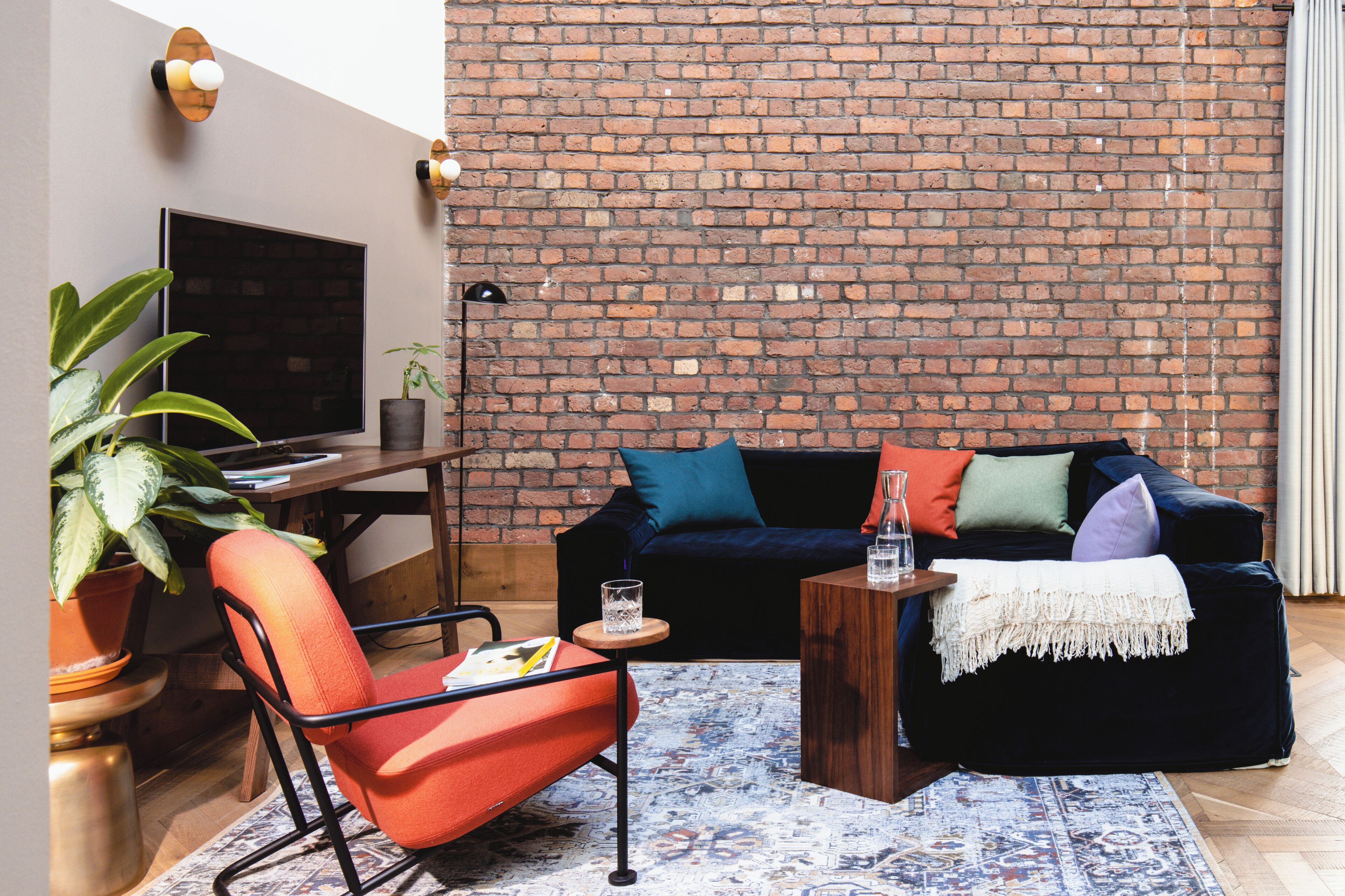 Een woonkamer met een bakstenen muur, een bank, een stoel, een salontafel, een televisie en een plant.