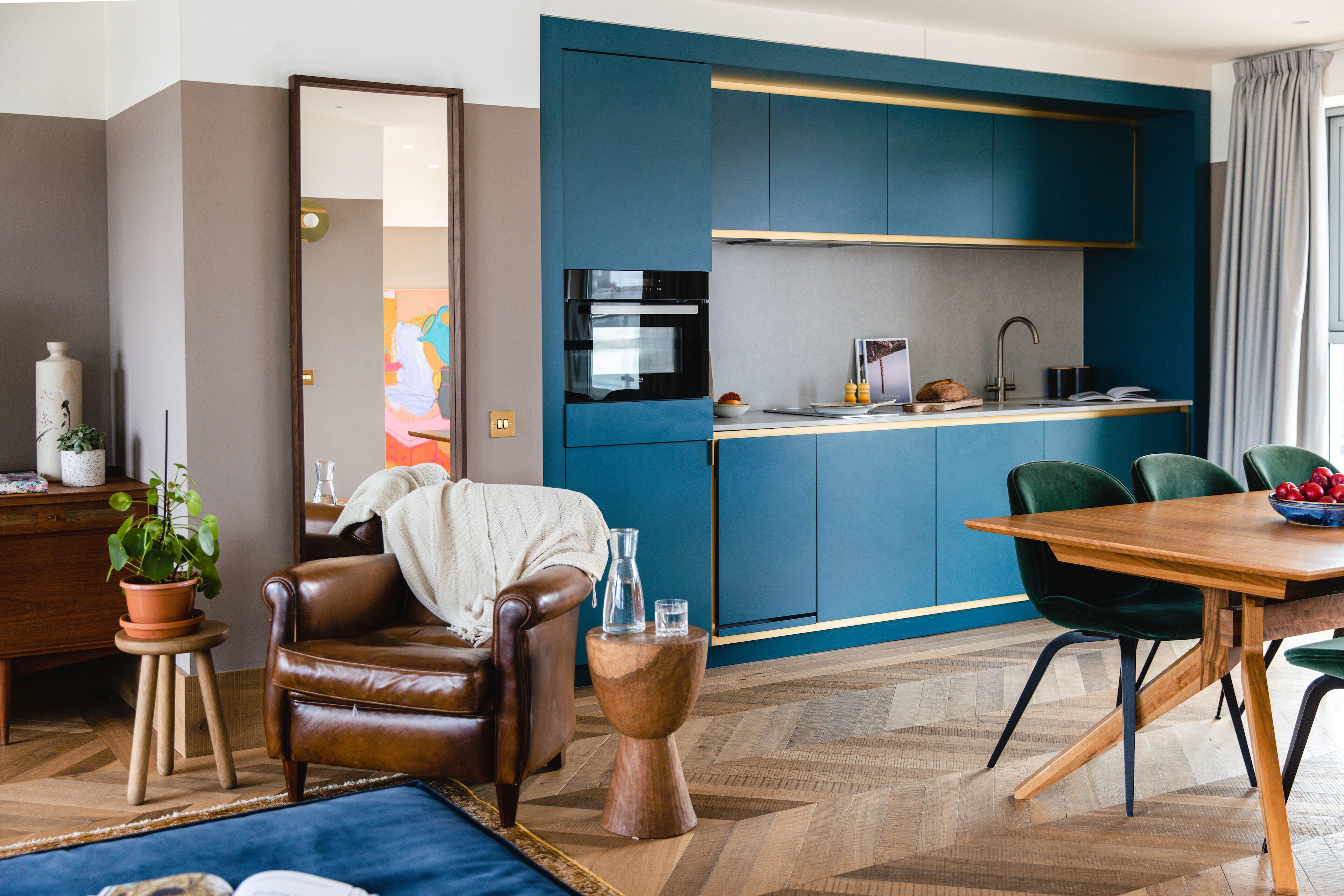 Una cocina moderna con armarios azules, un comedor con mesa y sillas de madera, y una sala de estar con sofá de cuero y una mesita auxiliar.