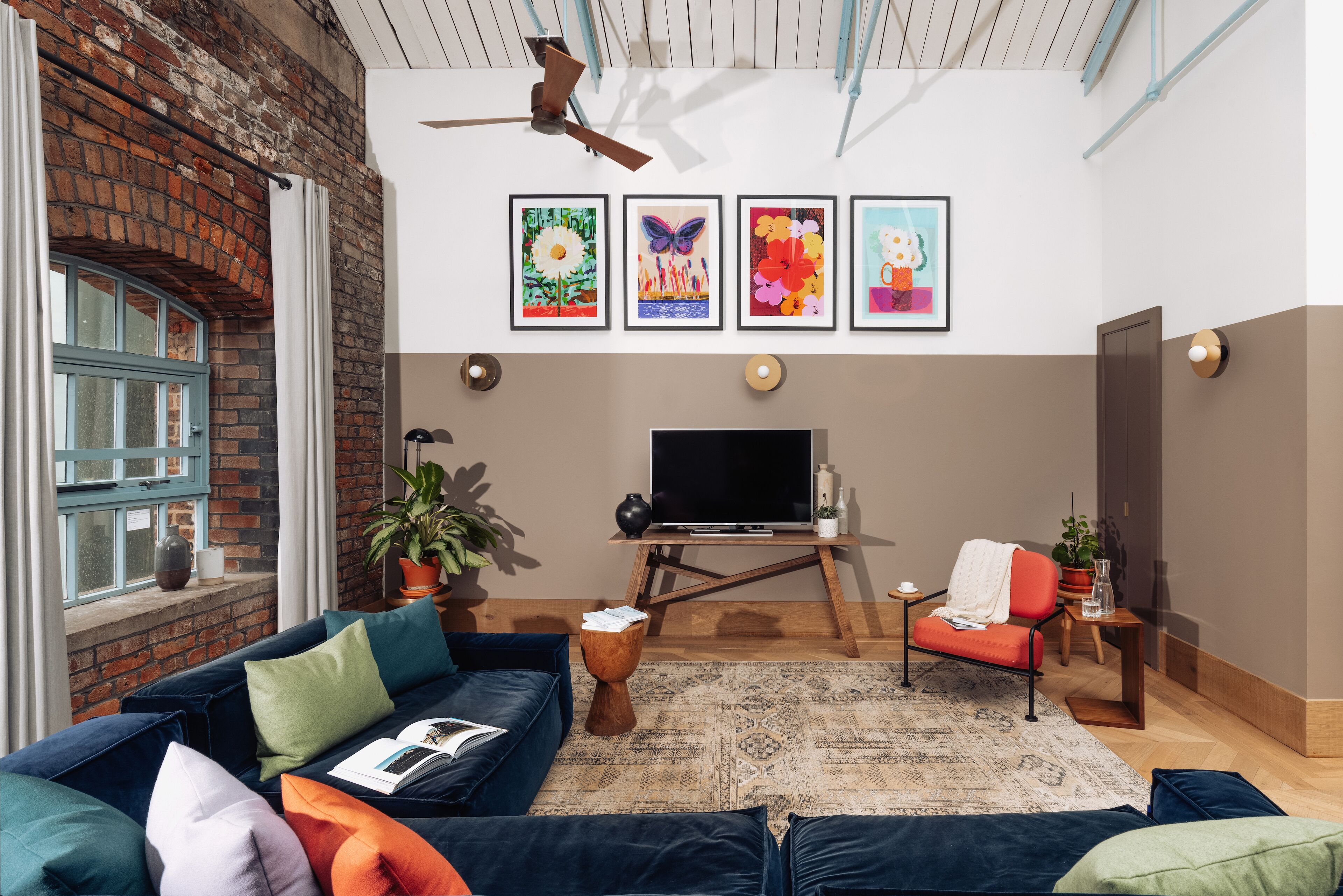 A cozy living room with a brick wall, a blue sofa, a TV, and artwork on the wall.