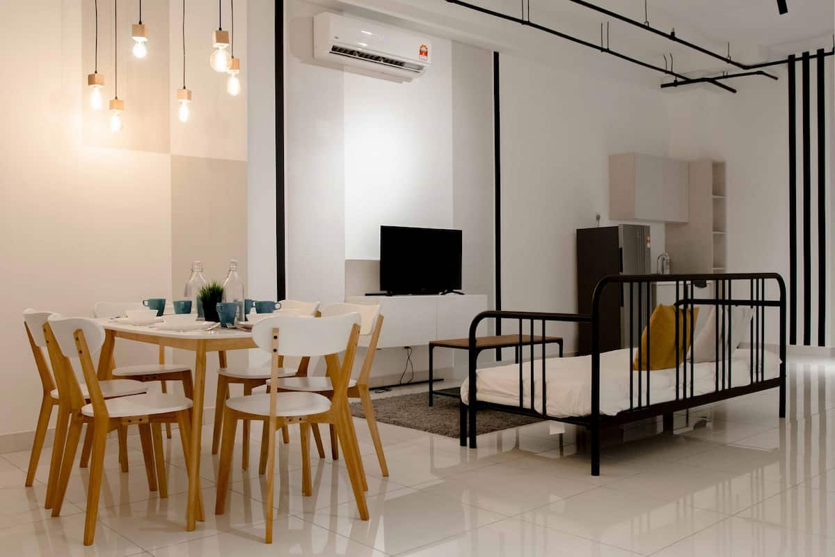 A modern, well-lit room with a dining table, chairs, a black metal bed frame, and a television.