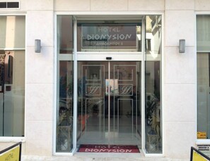A hotel entrance with a glass door, a sign reading "HOTEL DIONYSION," and a red mat at the entrance.
