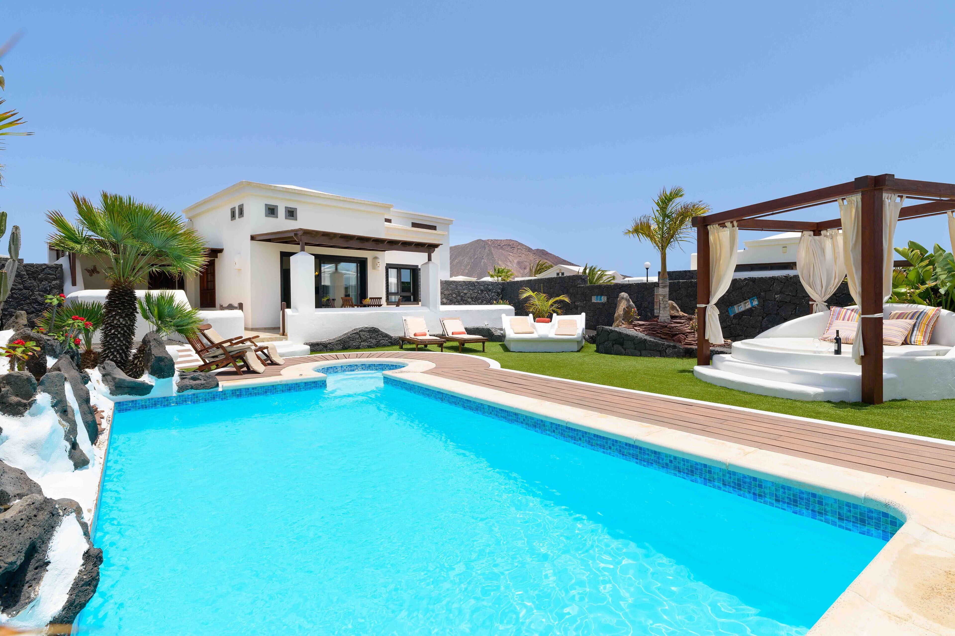 A modern pool area with a clear blue pool, lounge chairs, and a pergola with cushions.