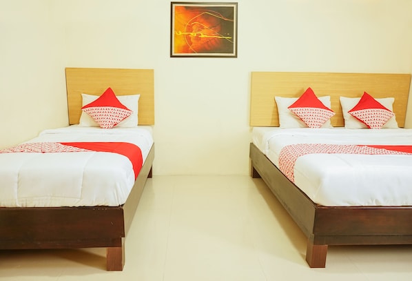 Deux lits jumeaux identiques, avec des têtes de lit en bois, du linge de lit blanc et des coussins à motifs rouges.