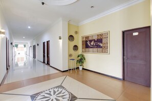 A hotel hallway with a tiled floor, a potted plant, a wall-mounted clock, and a door with a sign.