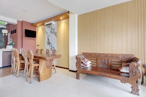 A modern living room with a wooden dining table, a sofa with intricate carvings, and a marble wall.