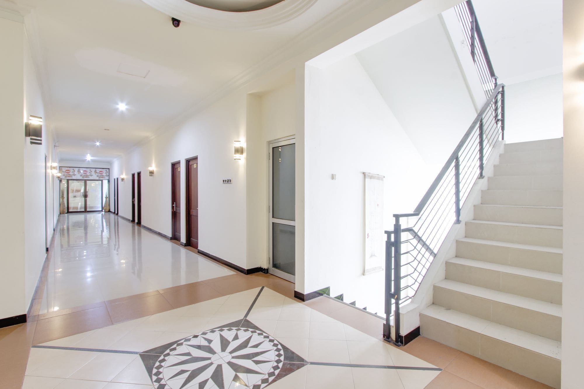 A hotel corridor with a central staircase, doors, and a patterned floor.
