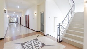 A hotel corridor with a central staircase, doors, and a patterned floor. - OYO 441 Namira Hotel Syariah (Pogung Lor)