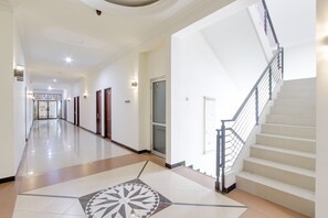 A hotel corridor with a central staircase, doors, and a patterned floor. - OYO 441 Namira Hotel Syariah (Pogung Lor)