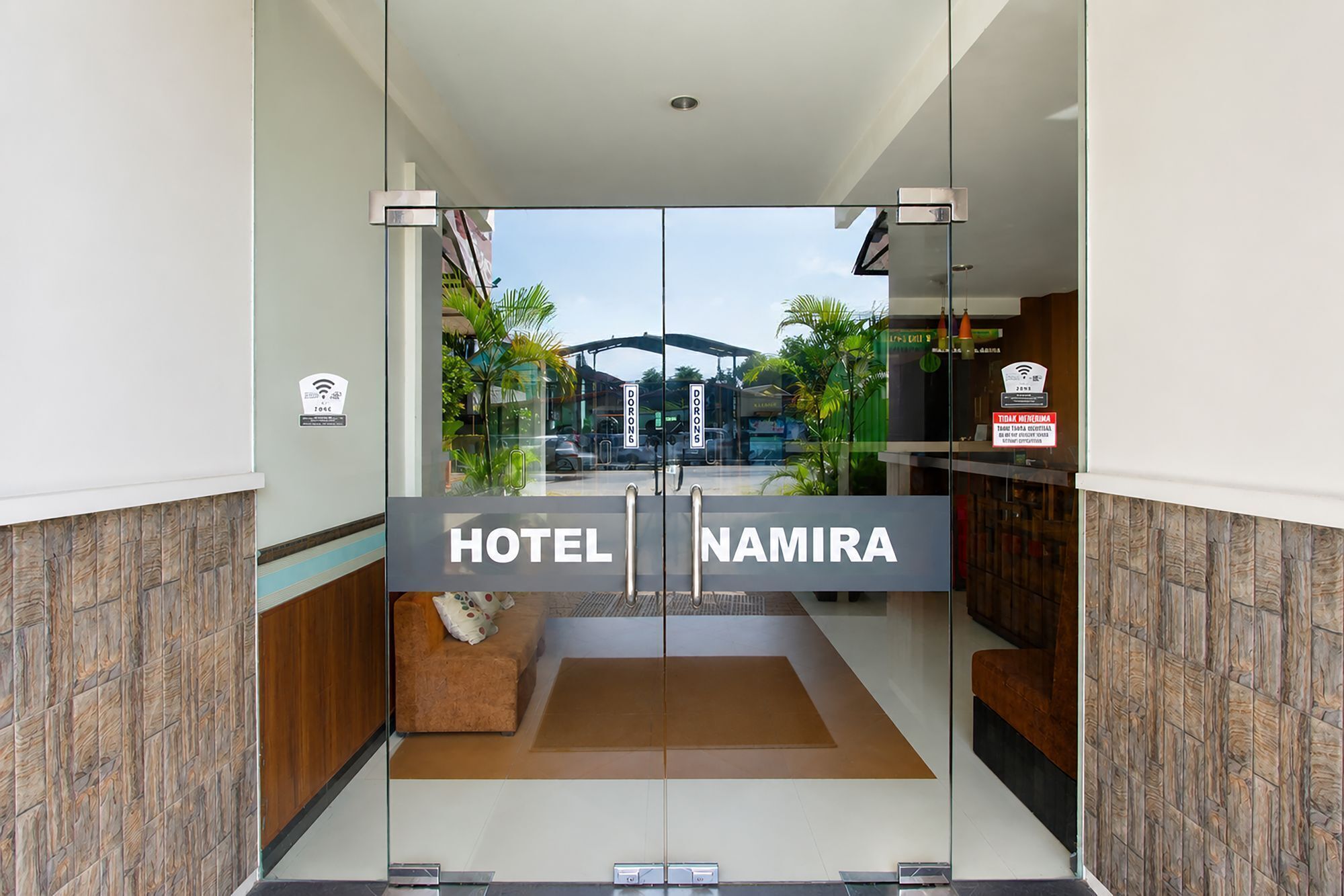Ein Hotel Eingang mit Glastür, einem Schild mit der Aufschrift 'HOTEL NAMIRA' und Blick auf die Straße.