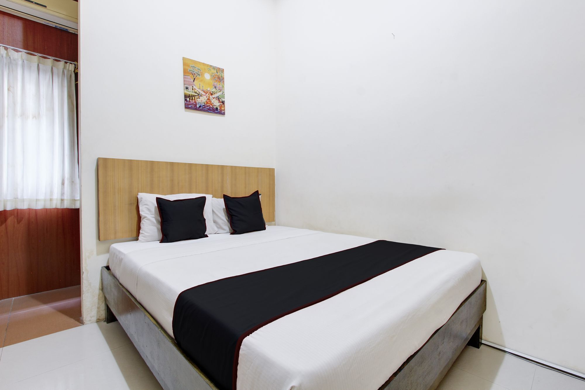 A hotel room with a bed, a headboard, and a painting on the wall.