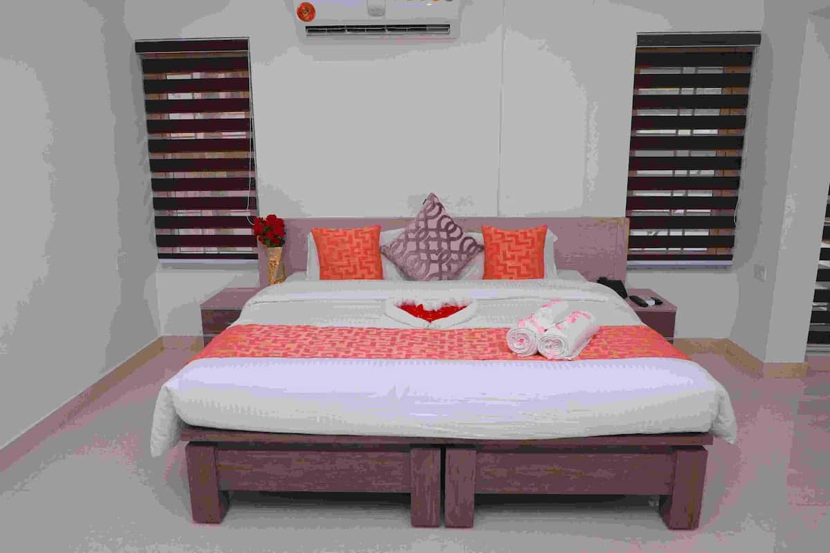 A bedroom with a bed, nightstands, a vase with flowers, and a window with blinds.