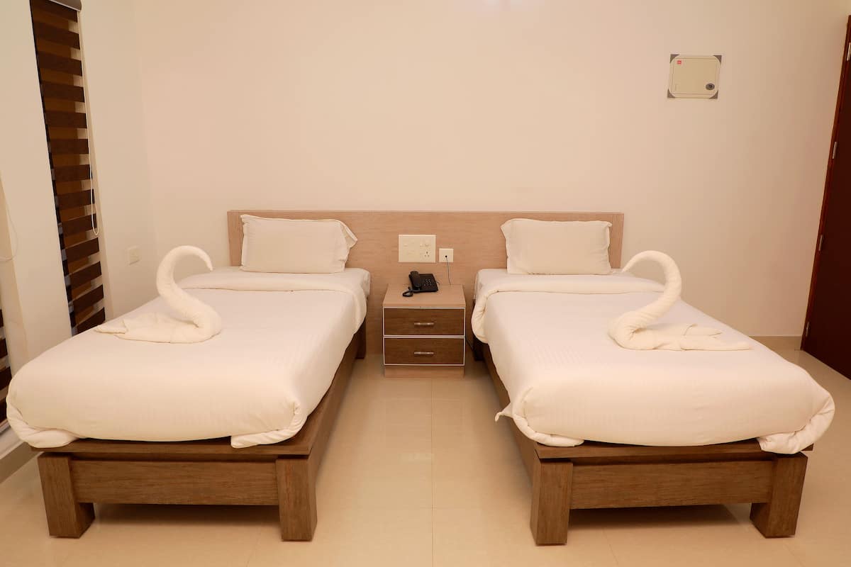 A hotel room with two beds, each with a wooden headboard and white bedding. There is a nightstand between the beds with a phone and a power outlet.
