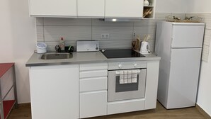 Eine kompakte Küche mit weißen Schränken, einem Backofen, einer Spüle und einem weißen Kühlschrank.