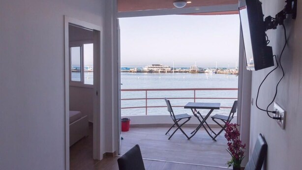 Ein Balkon mit Tisch und Stühlen, Blick auf das Meer und ein Gebäude in der Ferne.