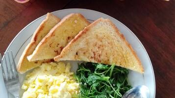 Un plato con tostadas, huevos revueltos y vegetales verdes, acompañado de un tenedor y una cuchara, sobre una mesa con mantel rojo.