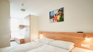A hotel room with a large bed, wooden headboard, bedside tables, a wardrobe, and a painting on the wall. - Grafenberg Resort by Alpeffect Hotels (Wagrain)