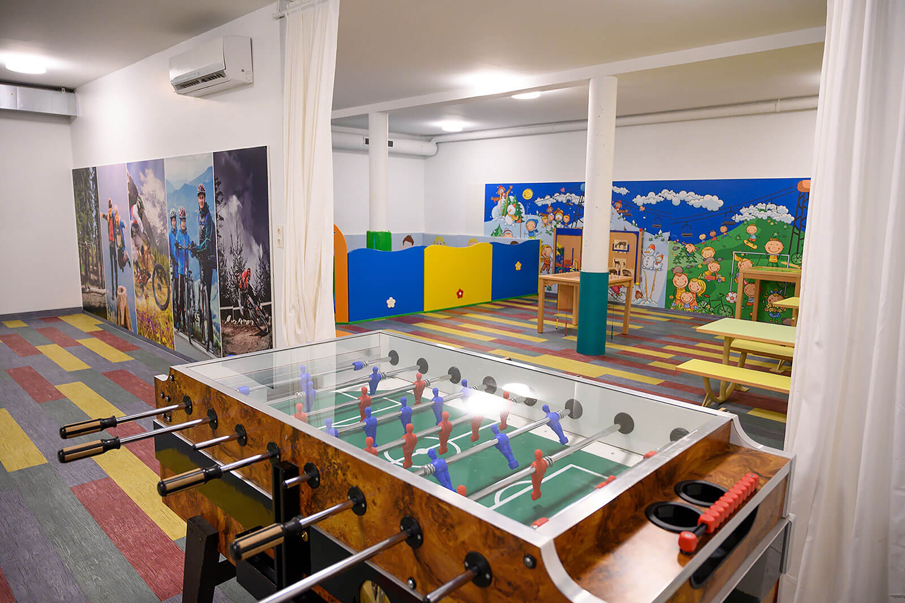 Een kamer met een tafelvoetbaltafel, een kleurrijk speelgedeelte en kindertekeningen aan de muren.