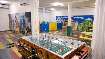 Een kamer met een tafelvoetbaltafel, een kleurrijk speelgedeelte en kindertekeningen aan de muren.