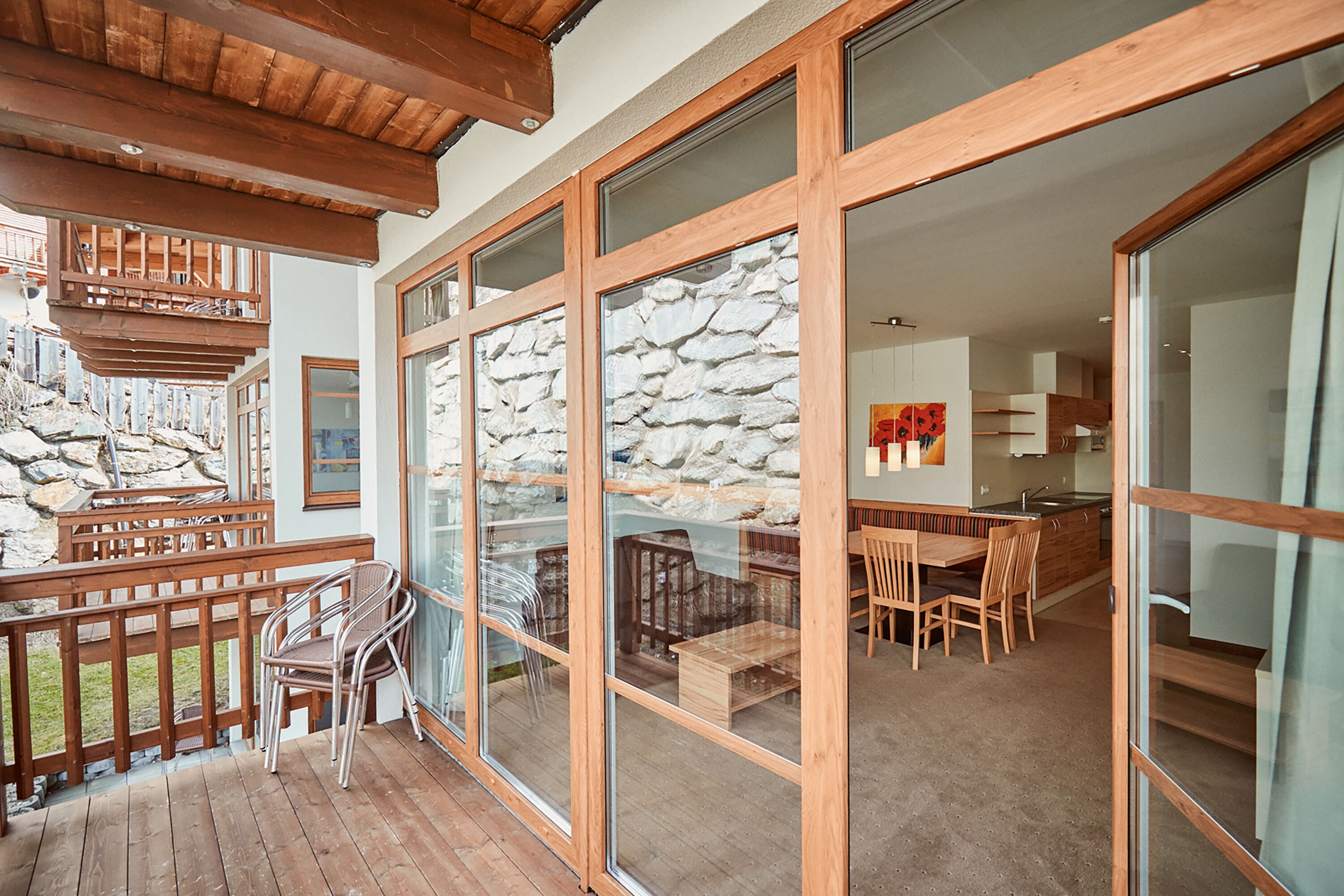 A spacious living area with a wooden deck, a stone wall, and a dining area with wooden furniture.