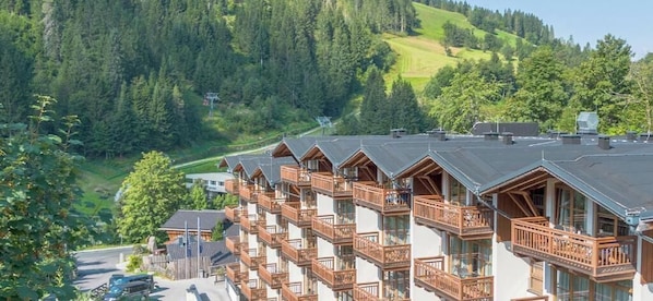 Una hilera de edificios tipo chalet de madera con balcones, frente a un paisaje de colinas boscosas.