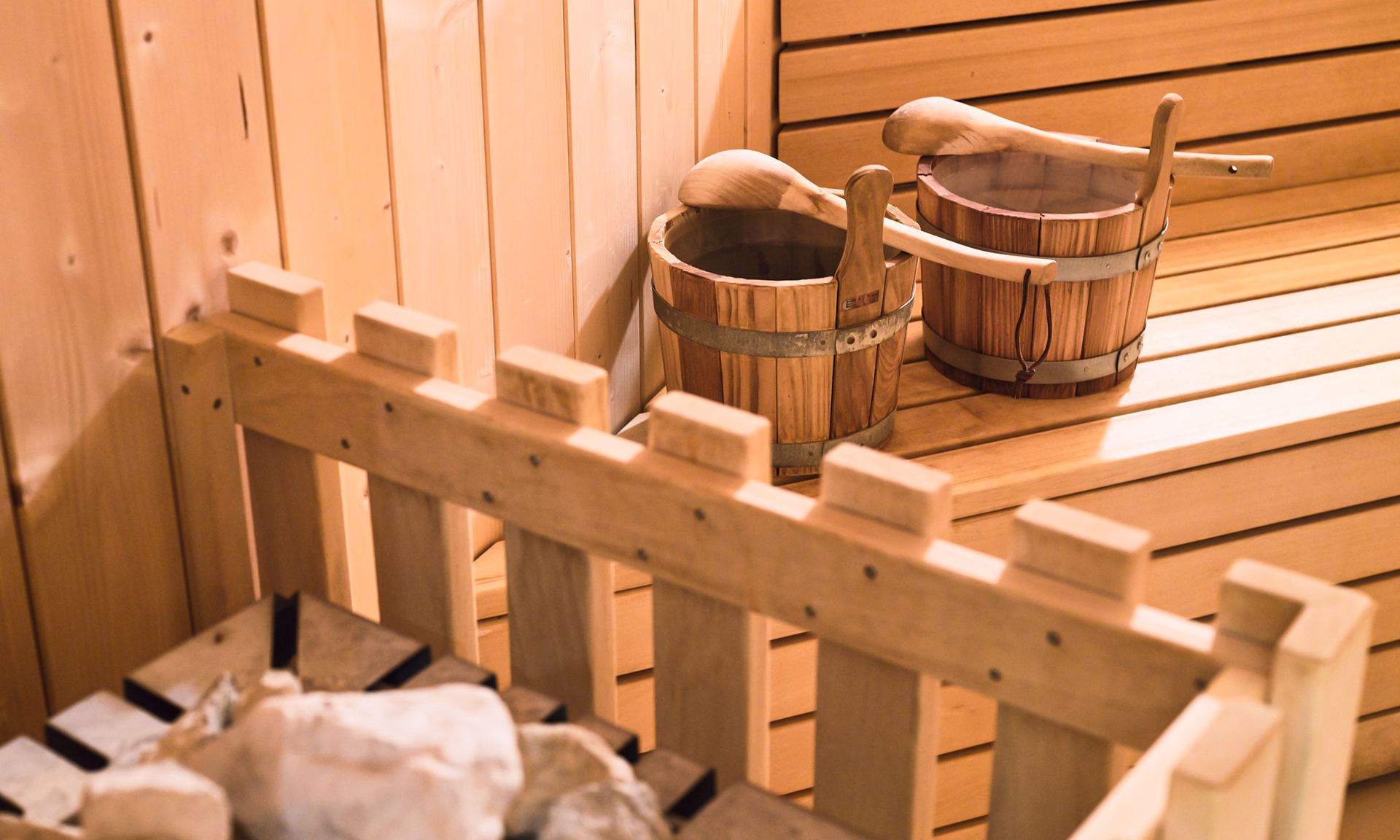 A wooden sauna bench with two wooden buckets and a wooden ladle.