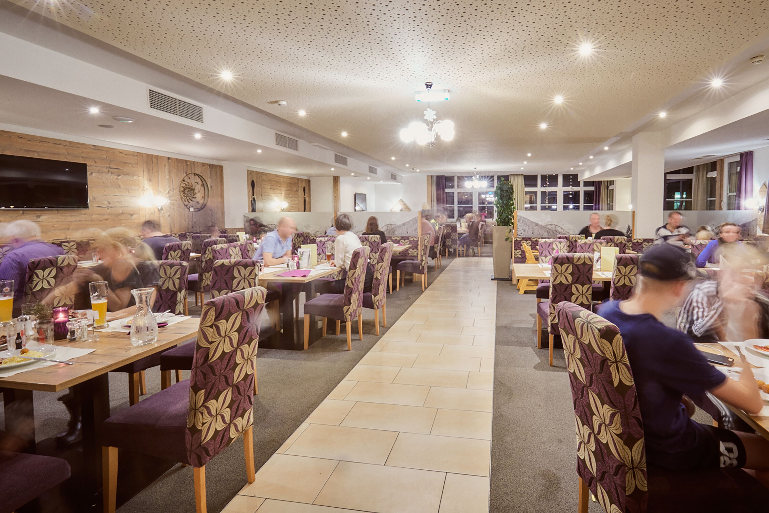 A spacious restaurant with multiple tables and chairs, a long counter, and a television mounted on the wall.
