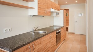 A modern kitchen with wooden cabinets, a granite countertop, a built-in oven, and a stainless steel sink. - Grafenberg Resort by Alpeffect Hotels (Wagrain)
