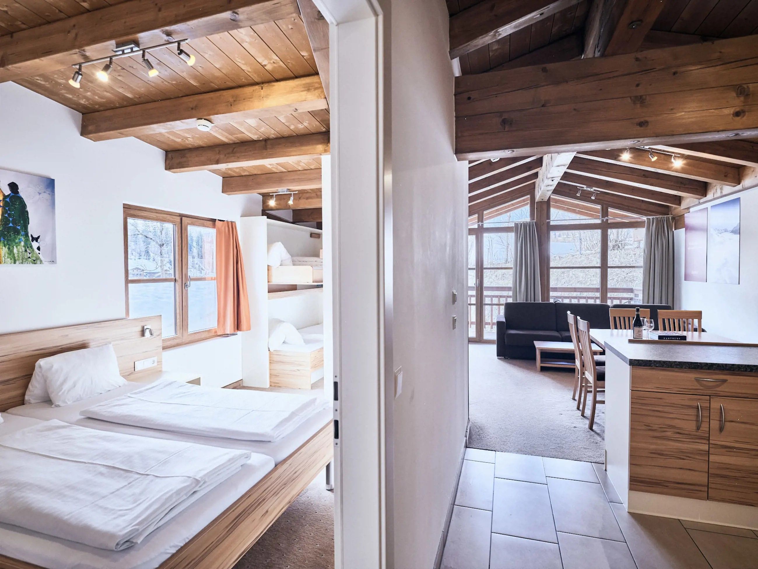 Ein modernes Interieur mit Holzbalkendecke, einem Bett mit weißer Bettwäsche, einer Couch und einem Essbereich mit Tisch und Stühlen.