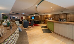 A modern interior with a curved ceiling, a reception desk, seating area, and a television screen. - Grafenberg Resort by Alpeffect Hotels (Wagrain)