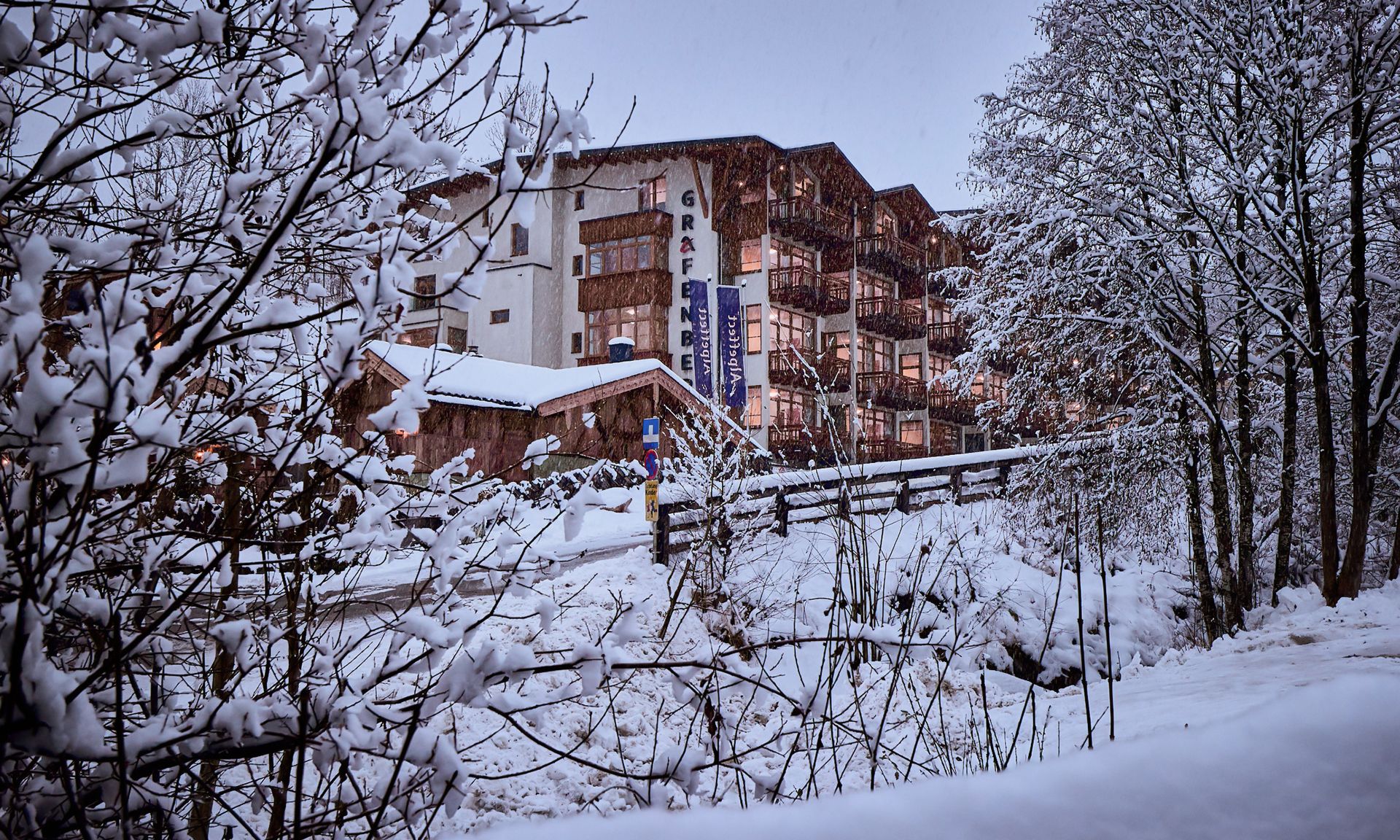 En byggnad med flera våningar och balkonger, omgiven av snötäckta träd och ett trästaket.