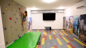 A climbing wall with colorful holds, a green padded mat, and a flat-screen TV on the wall. - Grafenberg Resort by Alpeffect Hotels (Wagrain)